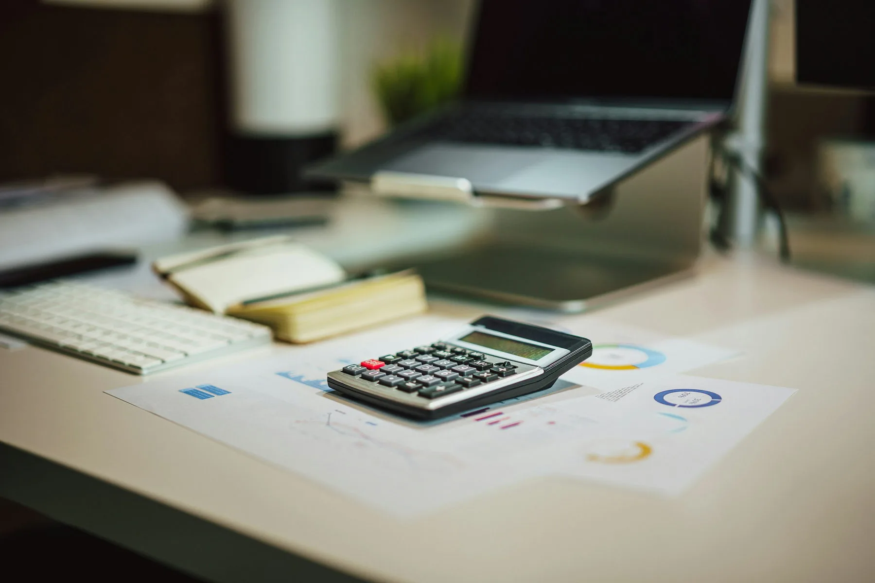 Calculator, notebook and reports on a desk beside a laptop