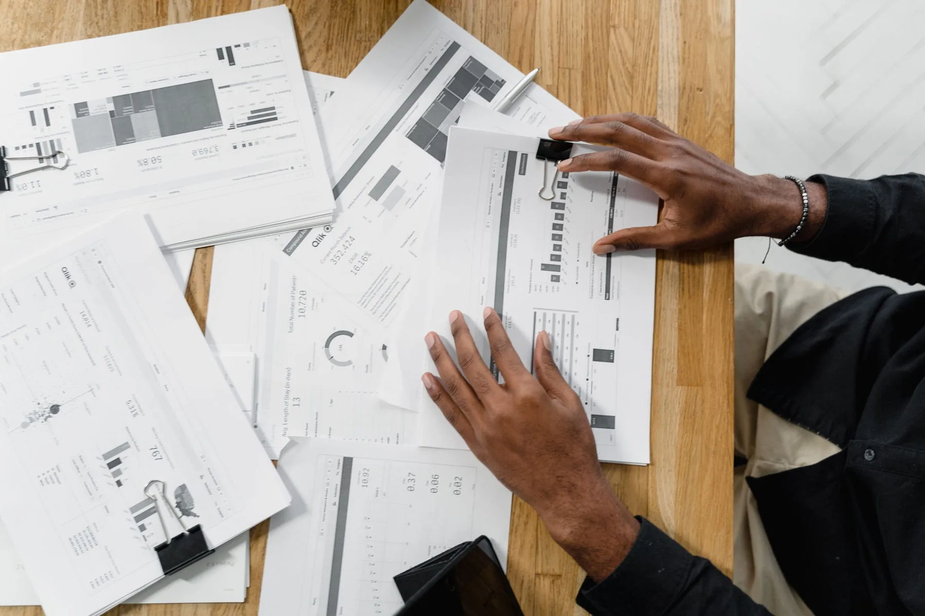 Hands working through printed financial documents on a timber desk